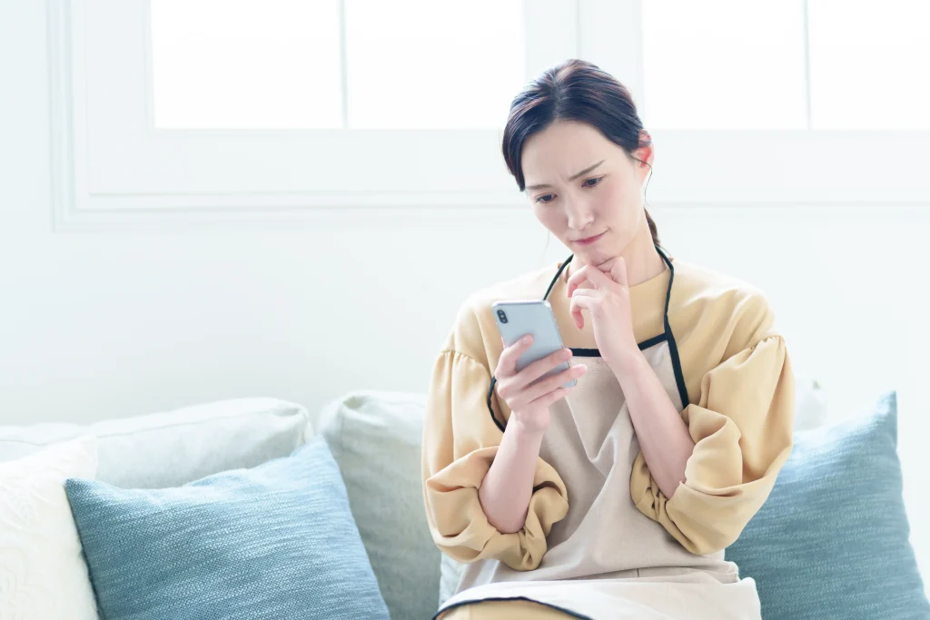 携帯画面を見ながら悩む女性